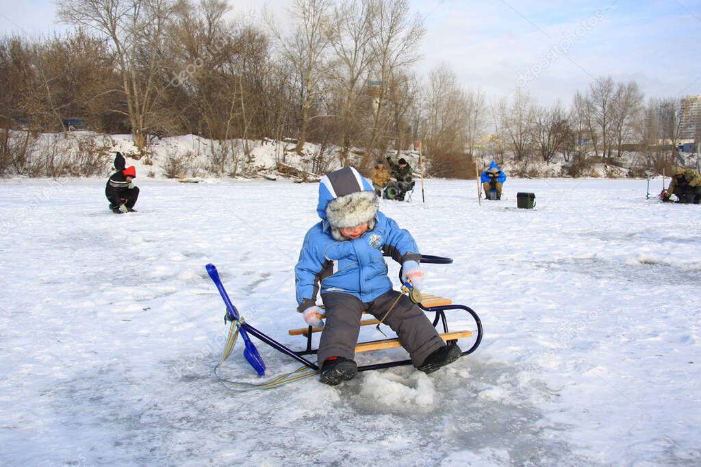 a little boy in winter clothes is fishing on a frozen lake