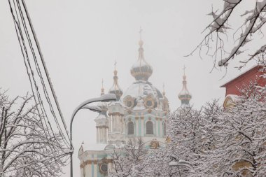 Karla kaplı evleri, ağaçları, arabaları olan kış şehirleri. Şehirde yoğun kar yağışı var. St. Andrew Kilisesi. Kiev. Ukrayna.