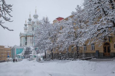Karla kaplı evleri, ağaçları, arabaları olan kış şehirleri. Şehirde yoğun kar yağışı var. St. Andrew Kilisesi. Kiev. Ukrayna.