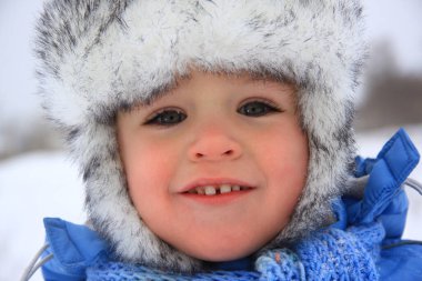 Kış giysileri içinde mutlu küçük bir çocuk. Arka planda, yakın plan portresi.