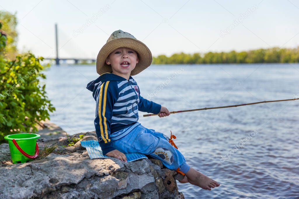 The little boy fishing on the river bank in spring