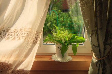 A bouquet of lilies of the valley in a vase on a windowsill