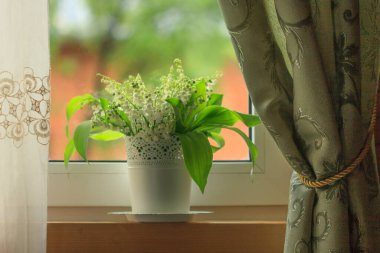 A bouquet of lilies of the valley in a vase on a windowsill