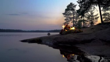 Gece yarısı gölün kıyısındaki bir ormanda yanan şenlik ateşi.