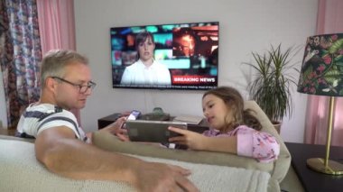 Orta yaşlı bir adam ve küçük kızı TV ekranının önünde..