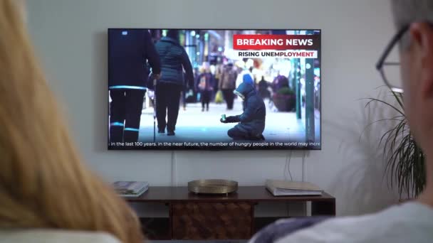 Familiepar som ser på TV Nyheter sittende på sofaen i stua sammen. – stockvideo