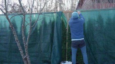 Soğuk ve soğuk bir sabahta bahçesini kışa hazırlayan bir adam bitkileri koruyucu kumaşla koruyor. Sakin mevsimsel yaşam tarzı atmosferi yumuşak doğal ışık ve erken kış havası.