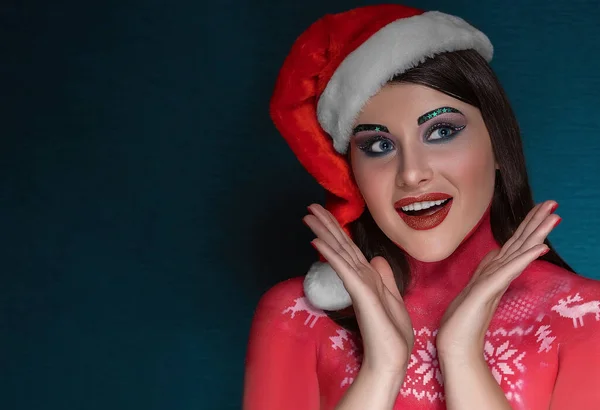 Una giovane donna bruna con un trucco artistico ideale e indossa un berretto di Babbo Natale è sorpresa, ammira — Foto Stock