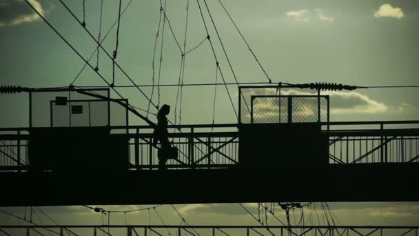 Silhouetten van mensen het oversteken van de spoorweg op oude metalen brug — Stockvideo