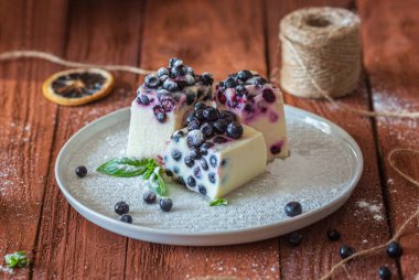 Kahverengi ahşap masada yabanmersini ve nane şekerli fırınlanmamış cheesecake dilimleri. Kırsal tarzda. Görüntüyü kapat