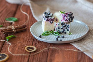 Kahverengi ahşap masa ve kumaş üzerinde yabanmersini ve nane şekerli fırınlanmamış cheesecake. Kırsal biçim