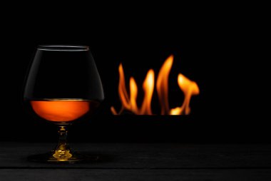 Arka planda şömine olan bir bardak viski.