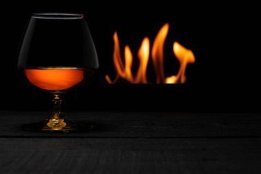 Arka planda şömine olan bir bardak viski.