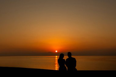 Gün batımında sahilde iki genç insanın silueti.