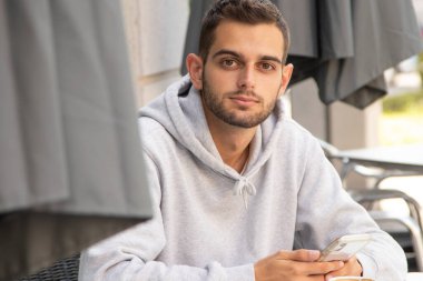 Kafe terasında oturan cep telefonlu genç adam.