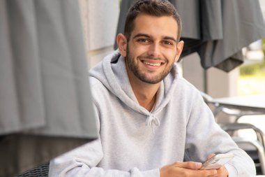 Kafe terasında oturan cep telefonlu genç adam.