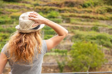 Sırtında şapkası olan kadın manzaraya bakıyor.