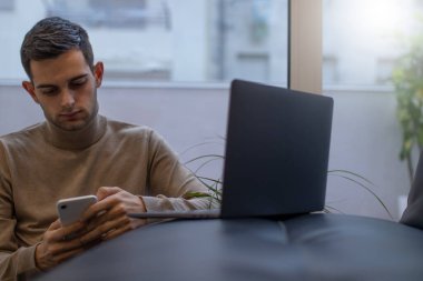 Adam evde dizüstü bilgisayar ve cep telefonuyla çalışıyor.