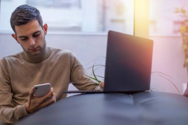 Adam evde dizüstü bilgisayar ve cep telefonuyla çalışıyor.