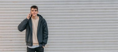 Genç bir adam şehir caddesinde kör bir adamın önünde cep telefonuyla konuşuyor.