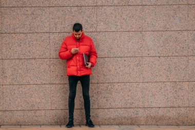 Duvardaki genç adam bilgisayarlı cep telefonuna bakıyor.