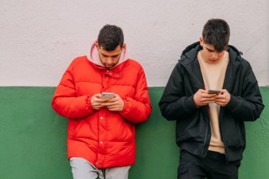 Duvara yaslanmış cep telefonlu gençler