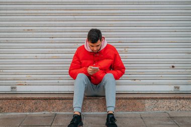 Cep telefonlu genç adam şehir caddesinde oturuyor.