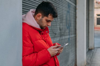 Sokakta duvara yaslanmış cep telefonu olan genç bir adam.