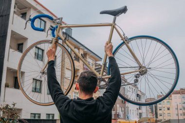 Genç adam şehirde kollarıyla bisikleti kaldırıyor.