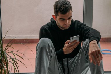 Evde cep telefonu yerde oturan genç adam.
