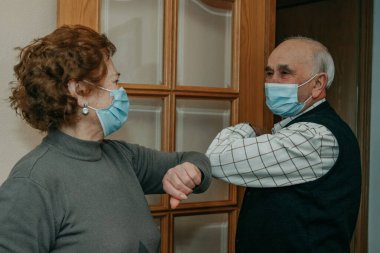 Büyükbaba ve büyükbaba Coronavirus salgınında birbirlerini maskeyle selamlıyorlar.