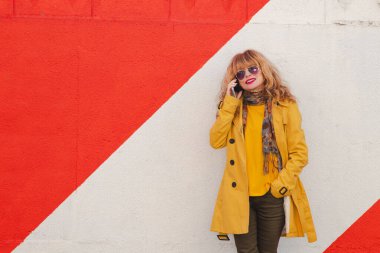 Duvarında kırmızı beyaz bantlı cep telefonu olan bir kadın.