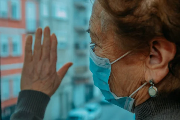 Senior Kvinna Med Ansiktsmask Instängd Hemma Med Handen Fönstret — Stockfoto