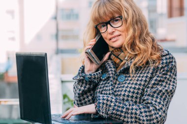 Sokakta cep telefonu ve bilgisayarı olan kadın.