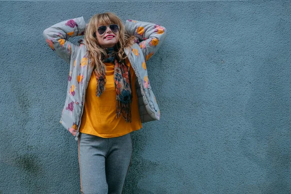 Güneş gözlüklü rahat kadın duvara yaslanıyor.