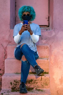 Sokakta cep telefonu ve maskesi olan Afro-Amerikalı kız.