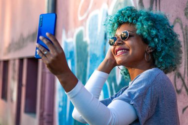 Gülümseyen Afro-Amerikalı kız video çekiyor ya da cep telefonuyla fotoğraf paylaşıyor