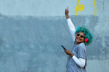 Afro-Amerikan kadın sokakta dans ediyor telefon ve kulaklıkla gülümsüyor.