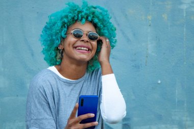 Sokakta cep telefonuyla gülümseyen Afro-Amerikan kadın.