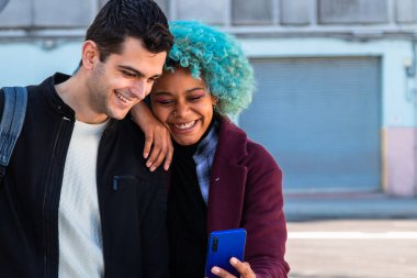 Gülümseyen genç çift cep telefonuna bakıyor.