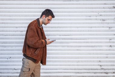 Genç adam sokakta yürüyor ve cep telefonuna bakıyor.