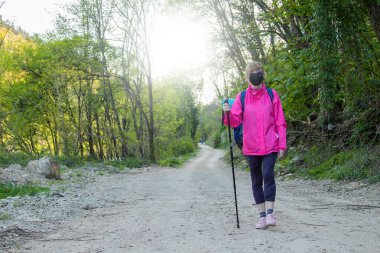 Maskeli ve sırt çantalı bir kadın. Yürüyüş ya da kutsal yolculuk.