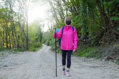 Maskeli ve sırt çantalı bir kadın. Yürüyüş ya da kutsal yolculuk.