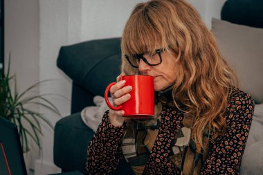 Evde bilgisayarlı bir kadın kahve içiyor.