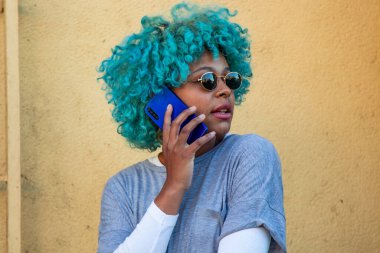 Güneş gözlüklü Afro-Amerikalı kız cep telefonuyla konuşuyor.