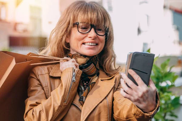 Glimlachende Vrouw Met Boodschappentassen Zoek Naar Mobiele Telefoon — Stockfoto