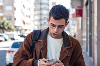 Şaşırmış bir adam sokakta cep telefonuna bakıyor.