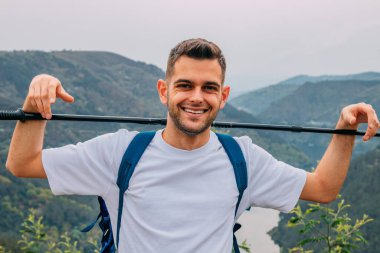 Gülümseyen genç adam doğa yürüyüşü yapıyor.