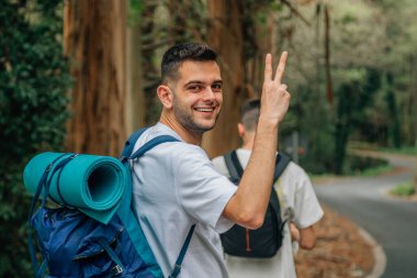 Doğada seyahat eden genç insanlar zafer işaretiyle gülümsüyor.