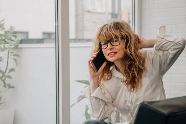 Evde cep telefonuyla konuşan yetişkin ya da yaşlı bir kadın